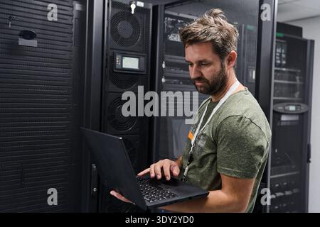 IT technician working on laptop in a data center server room checking network equipment Stock Photo