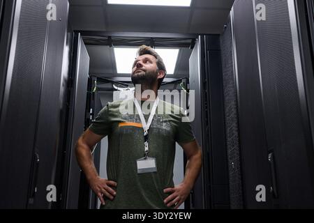 IT technician inspecting server racks in a data center under bright overhead lights Stock Photo