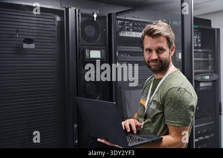 IT technician working on laptop in a server room data center maintaining network hardware and servers Stock Photo