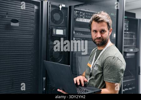IT technician working on laptop in server room of modern data center with racks and equipment Stock Photo