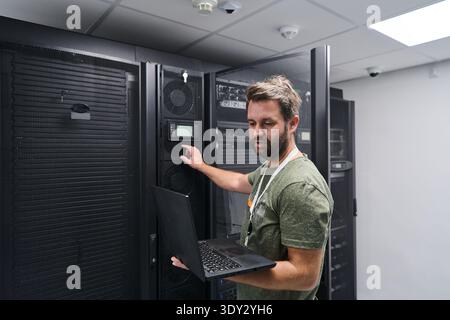 Data center technician monitoring servers with laptop in a server rack room performing IT maintenance Stock Photo