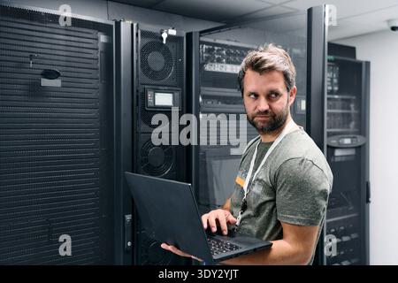 IT technician working on laptop in server room checking network equipment and data center racks Stock Photo