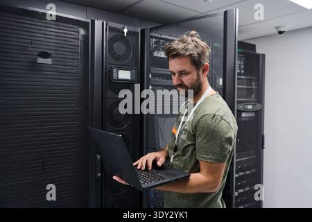 It technician working on laptop in server room performing network maintenance and hardware monitoring Stock Photo