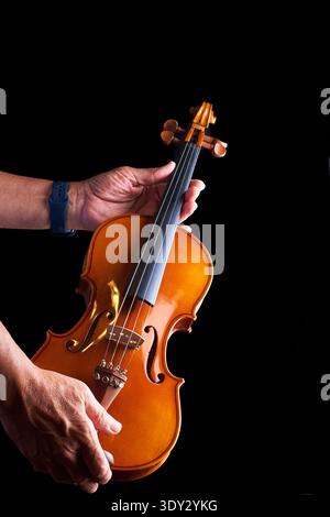 Person's hands holding a classical wooden violin on a black background Stock Photo