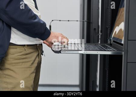 IT technician using a rack-mounted laptop console in a data center server rack for maintenance and monitoring Stock Photo