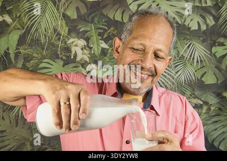 Smiling mature adult man pouring fresh milk into a glass Stock Photo