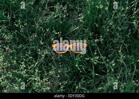 Bright orange 3D cinema glasses placed on fresh green grass outdoors. Entertainment and movie concept Stock Photo