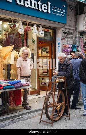 Vertical shot of an elderly man meticulously sharpens a knife using a traditional manual grinding wheel on a city sidewalk. Stock Photo