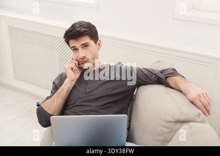 Serious young man at home with laptop and mobile Stock Photo