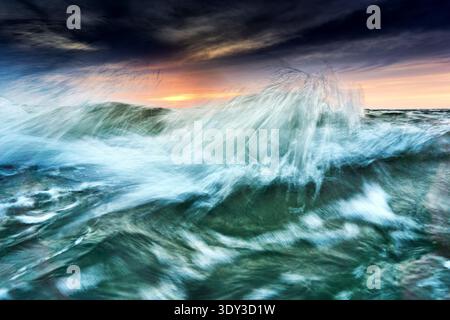 Dynamic long exposure photograph of ocean waves crashing at sunset, creating a vibrant, abstract display of water and light. The motion blur captures Stock Photo