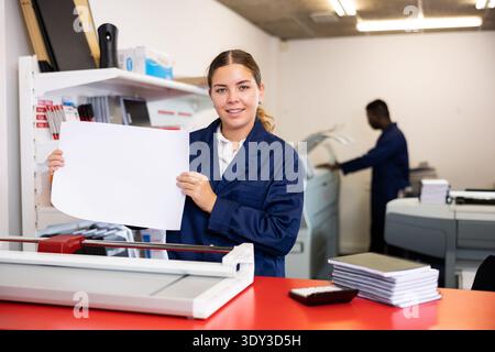 Happy young woman in uniform checking the print quality and accepting color proofs in the printer house Stock Photo