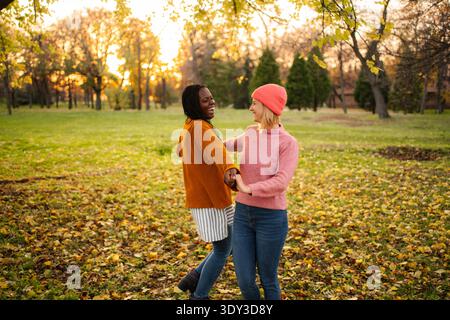 Diverse friends laughing and spinning together in autumn park Stock Photo