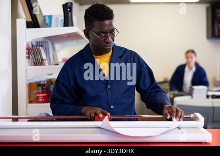 Serious print shop worker cuts paper on professional cutter Stock Photo