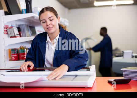 Work in printing house - woman cuts paper with professional cutter Stock Photo