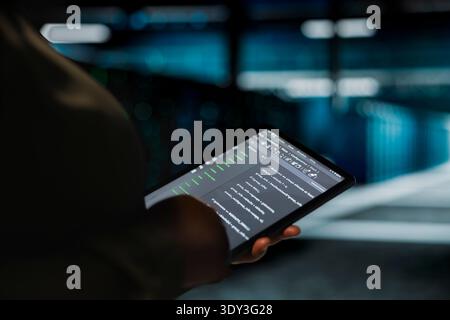 Data center computer scientist using tablet to optimize network infrastructure, planning capacity. Employee managing server room resources with device for improved reliability and uptime Stock Photo