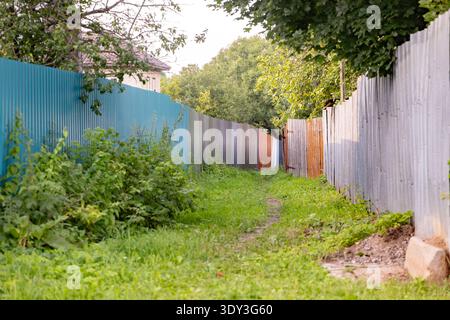 Rural dirt path leading through an alley of corrugated metal fences and green bushes Stock Photo