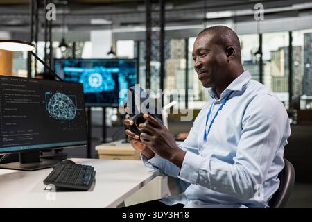 Smiling technician in office automating repetitive tasks using AI, listening music. Startup IT employee putting on audio headphones, using neural network on PC to speed up feature implementation Stock Photo