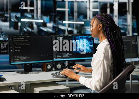 Data center admin running simulations for neural network forecasting, tracking performance. African american woman in server hub integrating machine learning APIs into software platforms Stock Photo