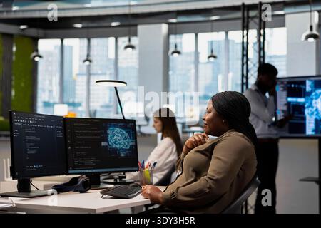 Happy developer speeding up tasks by following AI language model suggestions in office. Smiling african american woman relying on artificial intelligence LLM assistant to fix mistakes Stock Photo