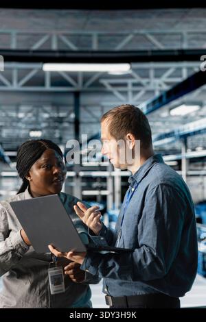 Server room coworkers troubleshooting server connectivity issues using software on notebook. Teamworking data center technicians upgrading enterprise networks hardware using laptop Stock Photo