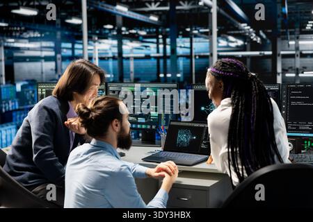 Team of engineers in data center doing brainstorming, troubleshooting server connectivity issues using AI. Coworkers collaborating in server room, auditing systems for vulnerabilities Stock Photo