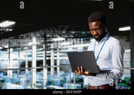 Smiling data center engineer on industrial platform works on neural network software tasks. Jolly african american technician visualizing large language model architecture, technical support. Stock Photo