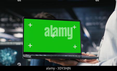 Close up of data center employee doing maintenance tasks on green screen laptop, ensuring optimal performance. Worker using mockup notebook to review diagnostics and apply patches Stock Photo