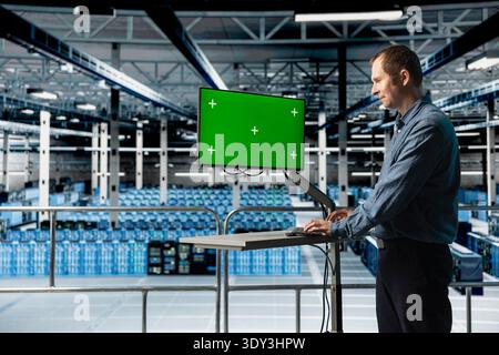 Happy IT professional in server room uses chroma key computer, upgrading hardware for increased storage capacity. Smiling data center engineer using isolated screen PC monitor to do optimizations Stock Photo