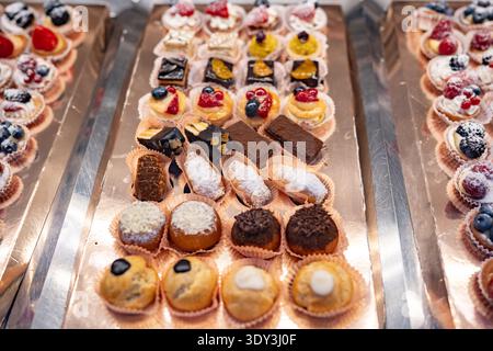 Displaying a variety of delicious mini pastries, cakes, and fruit tarts on silver trays Stock Photo