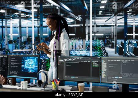 Programmer coding in data center, updating machine learning automation scripts. African american woman in server hub programming artificial intelligence algorithms, debugging equipment racks Stock Photo