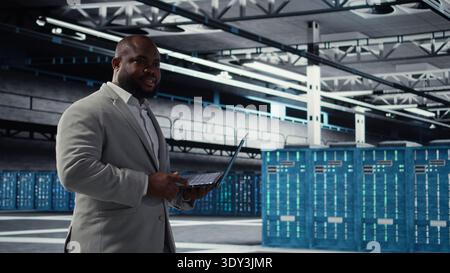 Cheerful data center system administrator reviews code for automation scripts. Jolly server room employee running diagnostics on equipment, doing predictive error detection, camera A Stock Photo