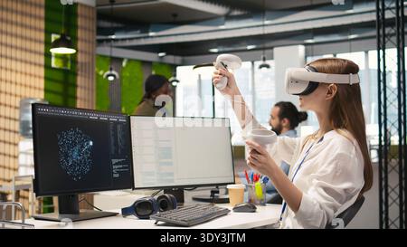 Junior dev using virtual reality at work, testing generative AI machine learning algorithms. Young woman wearing VR goggles equipment scaling productivity with AI large language model code, camera A Stock Photo