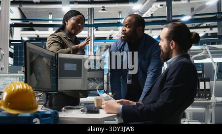 Multiethnic team of energy consultants review insight in solar panel plant, ensuring high standards in alternative energy production line. Quality control and manufacturing process. Camera A. Stock Photo