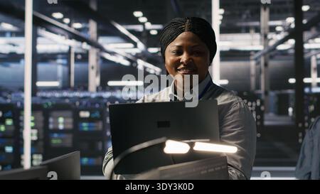 Portrait of happy technician next to data center colleagues review AI diagnostics. Cheerful IT specialist and coworkers analyze neural network performance to maintain operational reliability, camera A Stock Photo