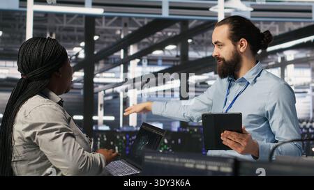 Server hub supervisor overseeing computer scientists improving neural network algorithms. Data center manager reviewing performance of employees doing checkup on infrastructure, camera A Stock Photo
