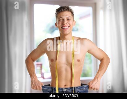 Happy man in his old jeans showing weight loss result at home Stock Photo