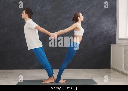 Couple training yoga in balance pose, standing back to back Stock Photo
