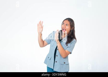 A young Southeast Asian woman looking up with a shocked face and open mouth, gesturing with hands against a clean white backdrop. Stock Photo