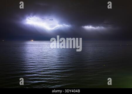 Nighttime thunderstorm over the Mediterranean Sea, featuring intense lightning strikes across stormy skies reflecting on the ocean surface Stock Photo