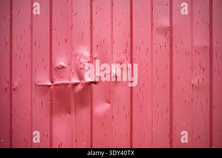 Dented red metal sheet wall showing damaged surface and vertical textures Stock Photo