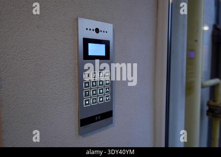 A door entry system with a keypad is mounted on a wall near the entrance. Users can enter numbers to gain access to the building or area. Stock Photo