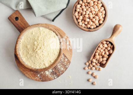 Chickpeas flour in wooden bowl with raw chickpeas on light background, top view Stock Photo