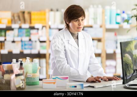 Female pharmacist working on computer at pharmacy counter Stock Photo