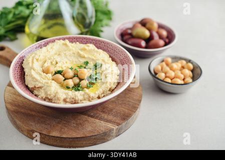Hummus in a ceramic bowl on a light background with pita bread and olives, closeup Stock Photo