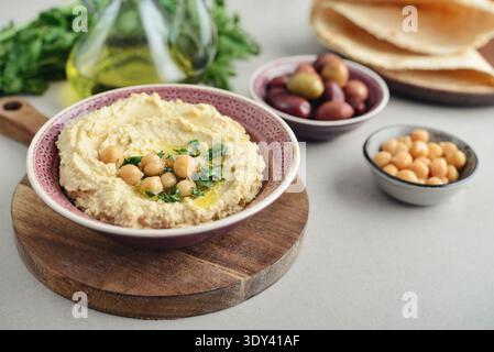 Hummus in a ceramic bowl on a light background with pita bread and olives, closeup Stock Photo