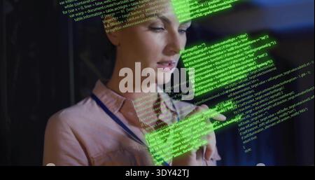 Holding phone, woman in dim office wearing pink shirt blue lanyard reading projected green code Stock Photo