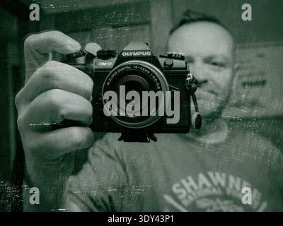 Artistic self-portrait of a photographer with an Olympus camera reflected in a mirror, styled with vintage texture and cinematic tones Stock Photo