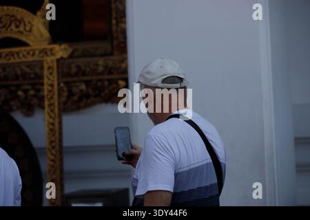 Senior man using smartphone taking photo in temple, nonverbal communication, tourists capturing travel moments with smartphone, rear view, at Wat Pho. Stock Photo