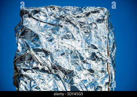 Crumpled aluminum foil surface texture shimmering in sunlight against blue background Stock Photo