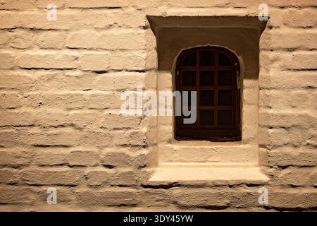 Grungy brick wall with small arched window providing old rustic architecture Stock Photo